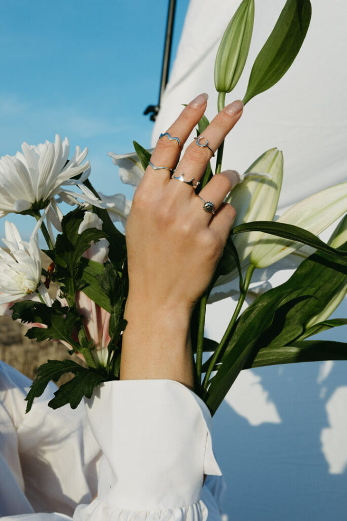 Mano femenina con anillos de Urpi Shop apoyada sobre flores